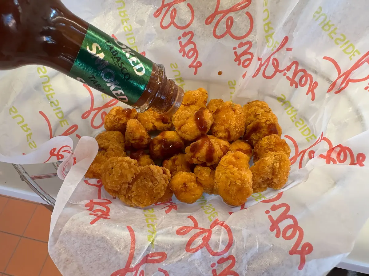 Pouring hot sauce on popcorn chicken